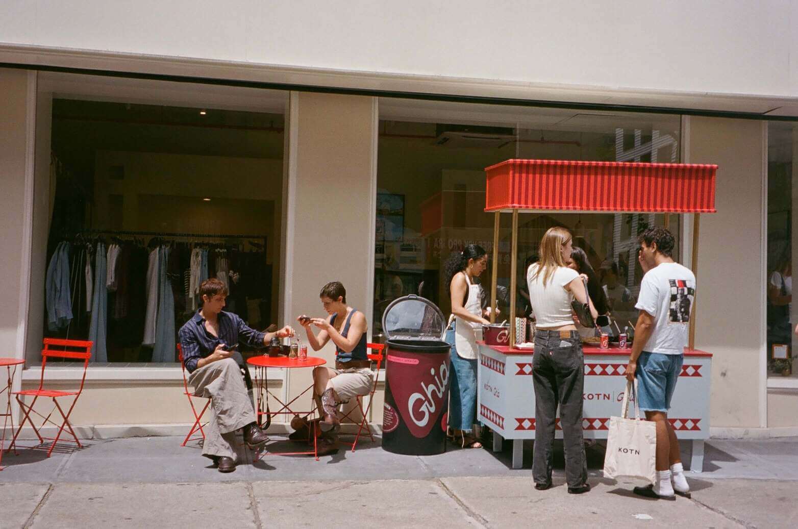 Pilar Adams People gather around a small outdoor ice cream stand with red chairs and tables in front of a clothing store on a sunny day. Communications & Event Strategist