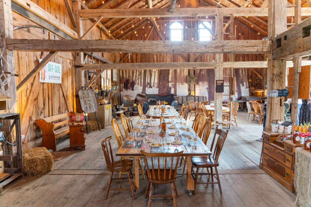 Pilar Adams A rustic wooden dining hall with a long table set for a meal, surrounded by wooden chairs, exposed beams, and warm ambient lighting. Communications & Event Strategist